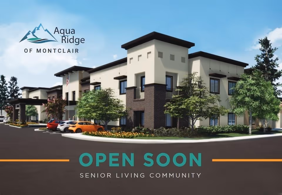 Exterior view of a modern senior living community building with multiple windows, surrounded by trees and parked cars under a clear blue sky. The building has a beige and dark brick facade with a flat roof.