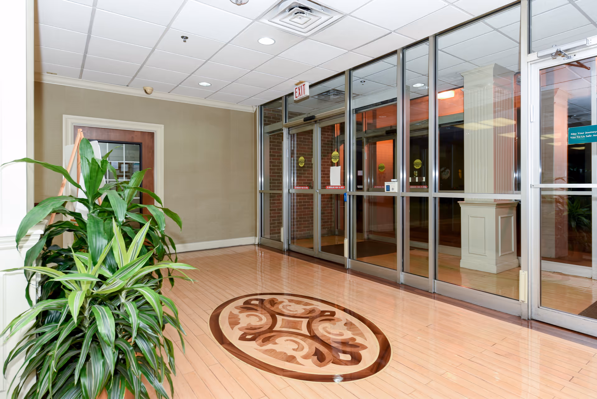 Lobby entrance with polished wood floor medallion, potted plant, and large glass entry doors.