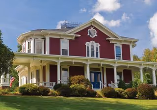 Red, two-story Victorian-style building with a wraparound porch and manicured lawn.