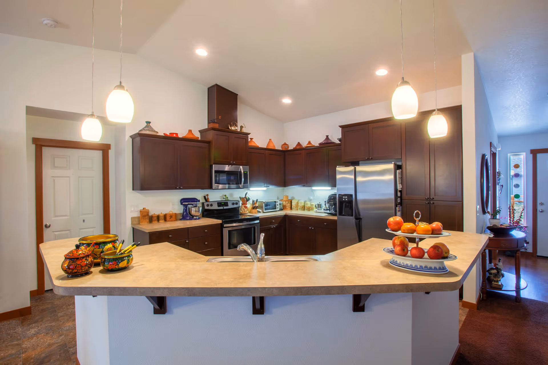 Bright modern kitchen with a large peninsula, stainless steel appliances, dark wood cabinets and pendant lights.