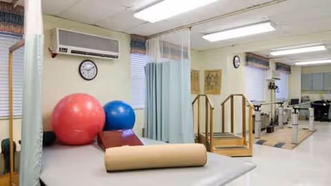 Rehabilitation therapy room with exercise balls, mat, curtain dividers, and equipment.