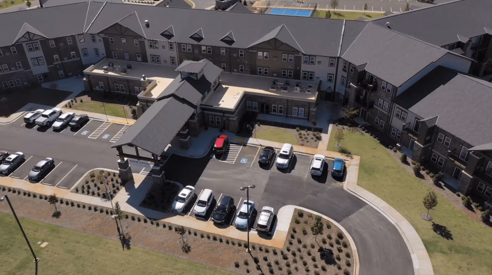 Aerial view of a three-story senior living building with a covered entrance, circular driveway and parked cars.