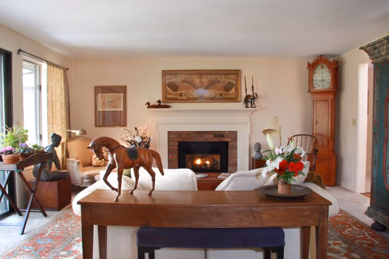 Cozy living room with a lit fireplace, sofa, console table topped with a wooden horse sculpture and flowers.