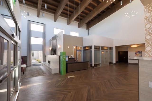 Spacious modern lobby with high exposed-beam ceiling, reception desk, tall windows and seating area.