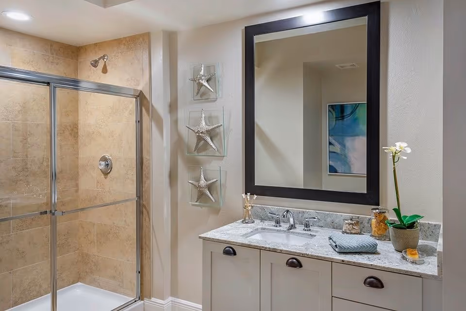 Modern bathroom with a glass-enclosed tiled shower, a vanity with marble countertop and large mirror, and decorative starfish on the wall.