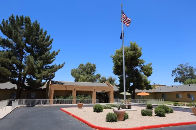 Front entrance of a single-story post-acute rehabilitation center with a flagpole and a landscaped circular courtyard under a clear blue sky.