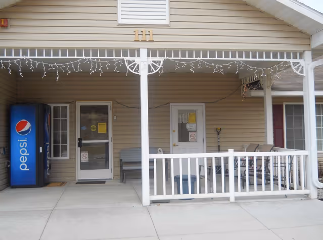 Front porch of a senior living facility with doors, seating, and a Pepsi vending machine.