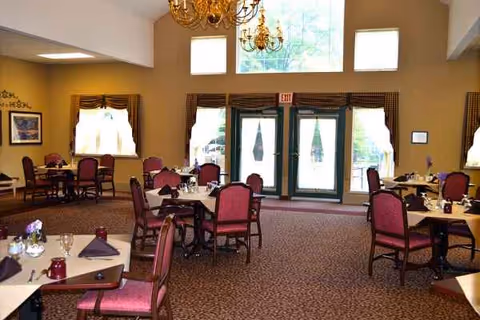 Dining room in a senior care center with round tables, burgundy chairs, and chandeliers.
