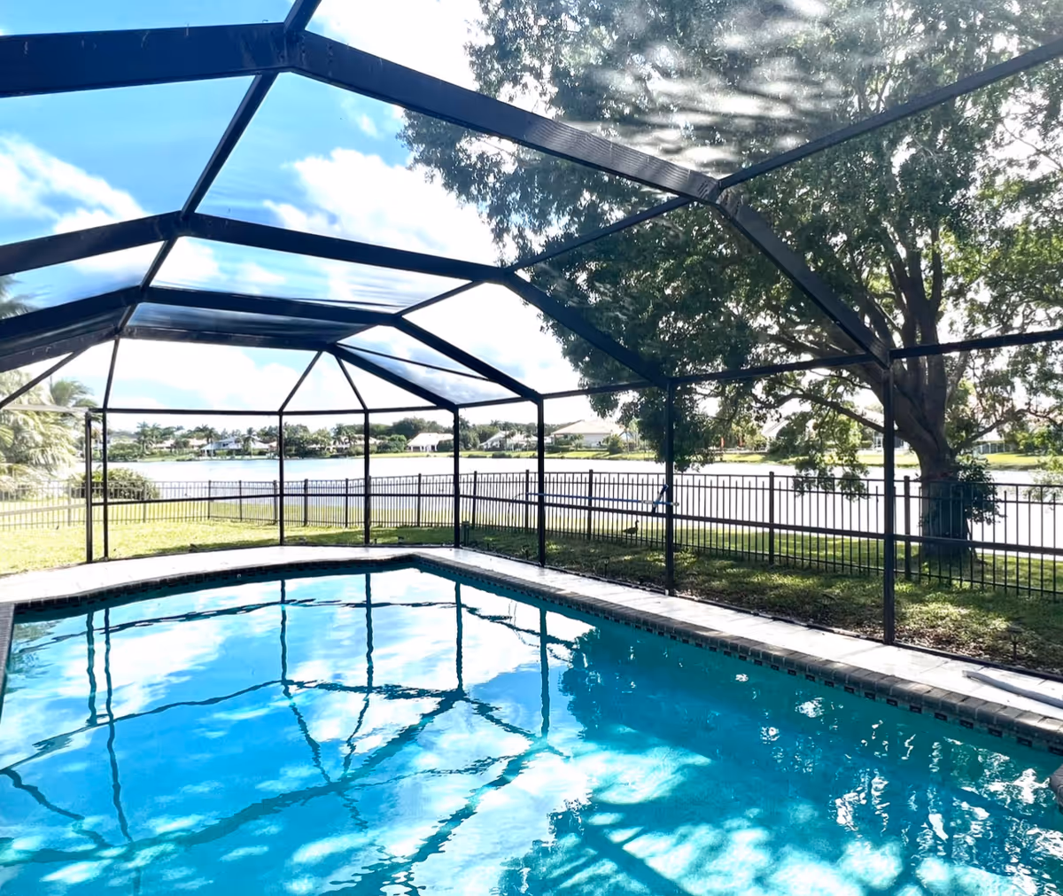 Screened outdoor swimming pool with a fenced yard overlooking a lake and trees.