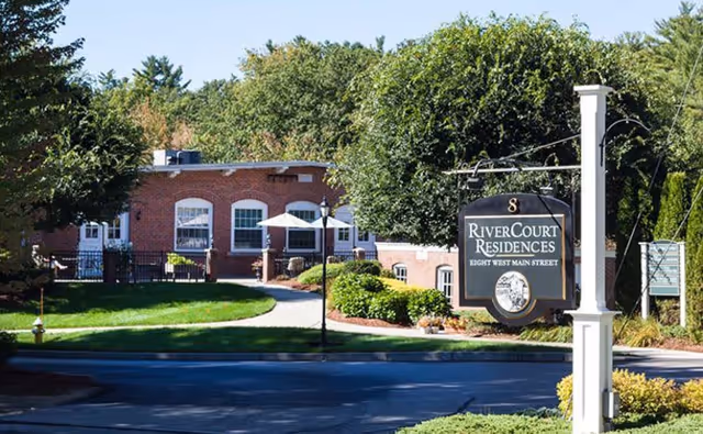 Front exterior of RiverCourt Residences with brick building, manicured lawn, and sign.