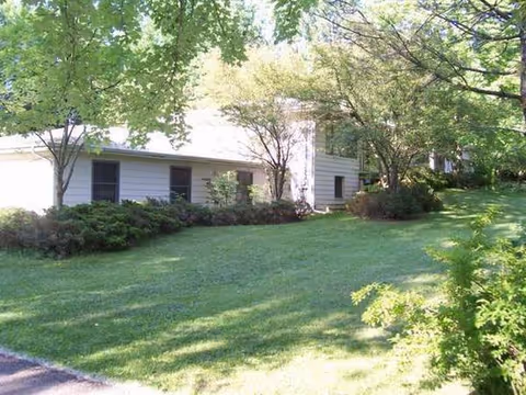A single-story white building sits beside a well-maintained green lawn with trees and shrubs.