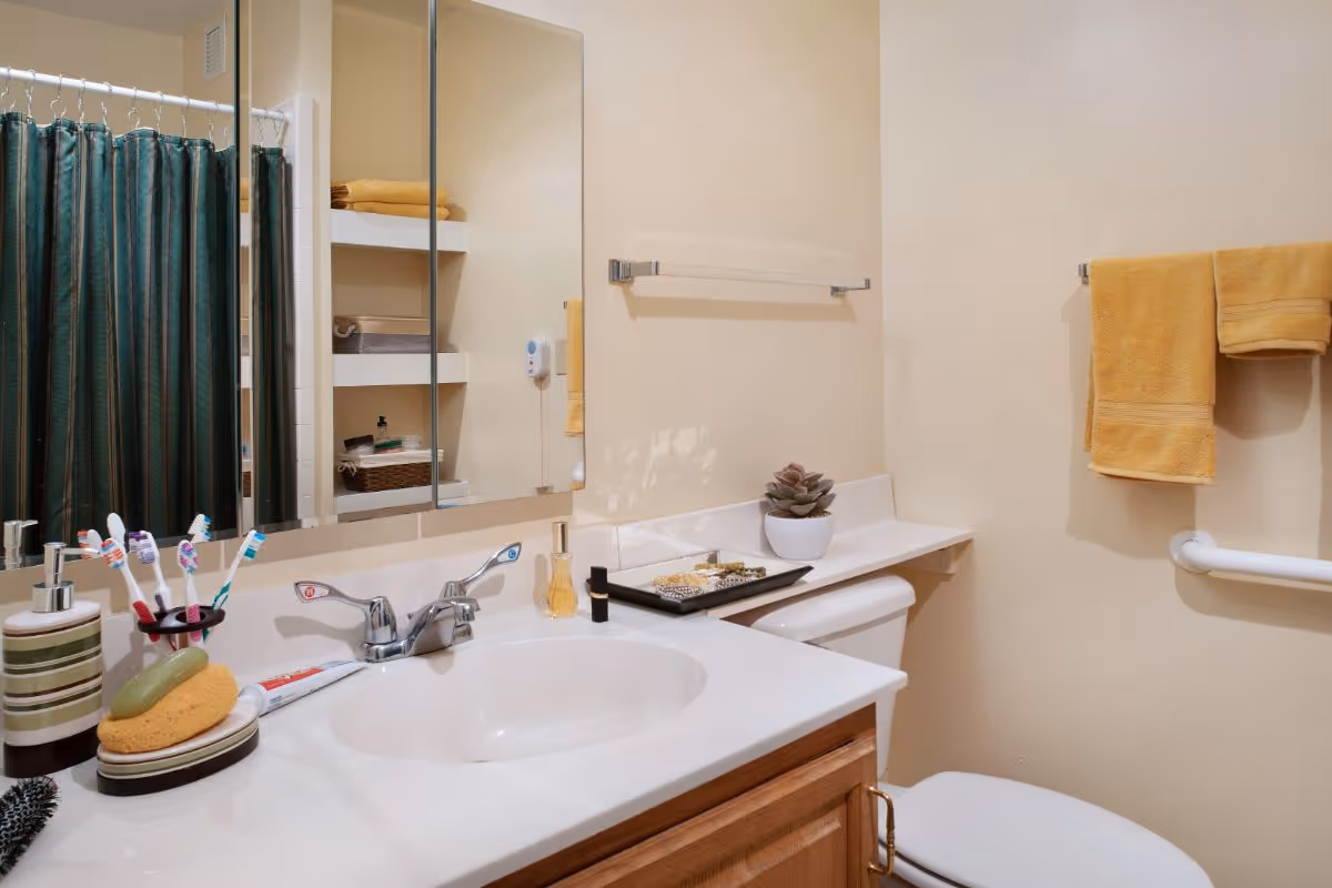Bathroom vanity with sink and mirror, toothbrushes and toiletries on the counter, yellow towels, and a green shower curtain.