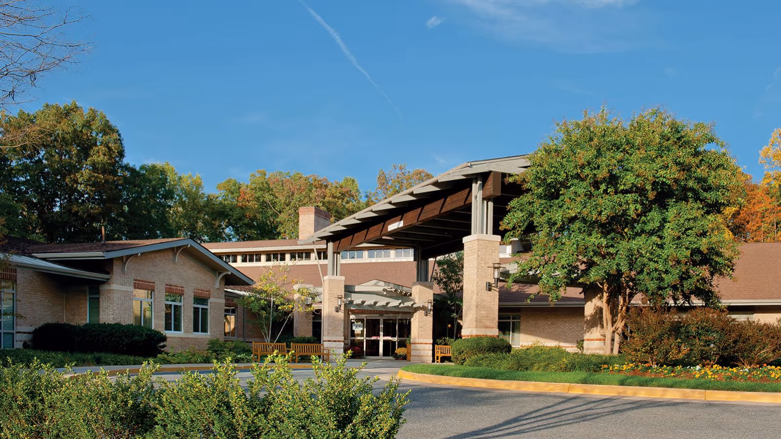 Front entrance of the Greenspring Senior Living Community with a covered porte-cochère, landscaped grounds and trees.