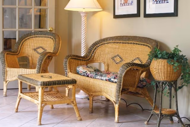 Wicker seating area with a loveseat, chair and ottoman beside a floor lamp and potted plant in a tiled room.