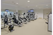 Interior fitness room with several cardio machines (recumbent bikes and ellipticals), a mirrored wall, and wall-mounted TVs.