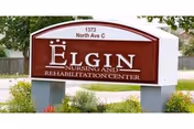 Outdoor sign for Elgin Nursing and Rehabilitation Center located at 1373 North Ave C, surrounded by grass and some plants with a residential fence and houses in the background.