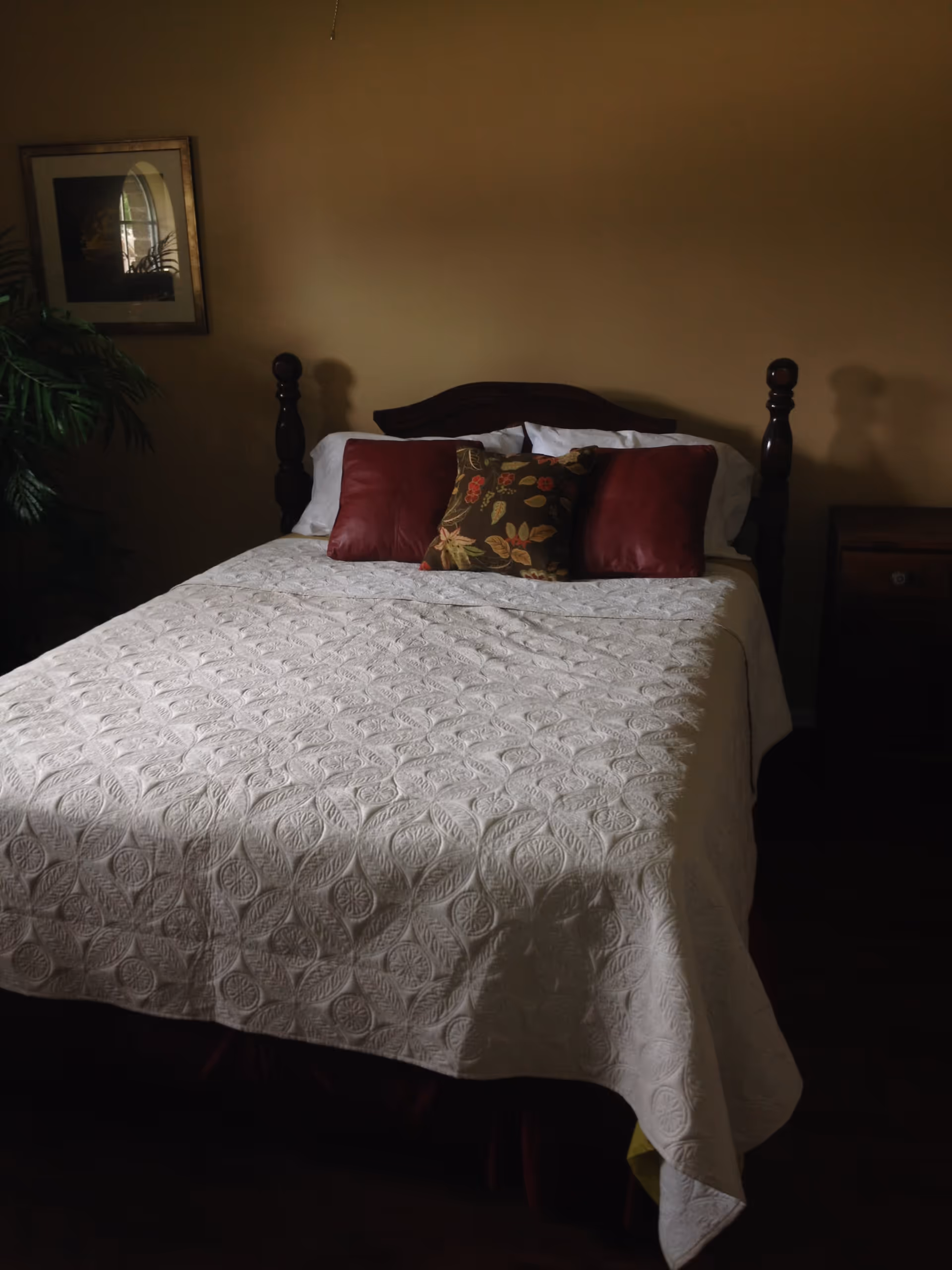 A neatly made bed with a white quilt and decorative pillows in a softly lit bedroom.