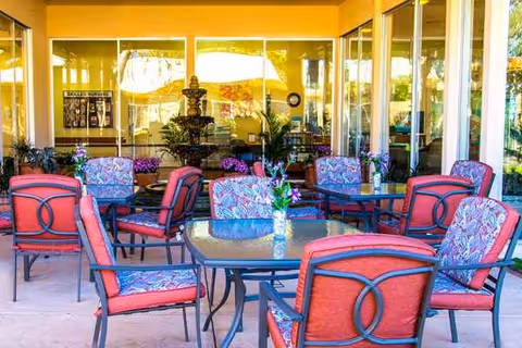 Outdoor patio at Buena Vista Care Center with red cushioned chairs, glass tables, and potted plants.