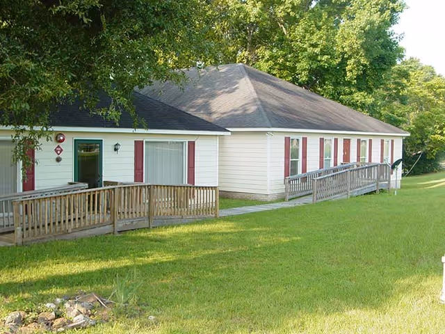 Single-story beige building with red shutters and a wooden ramp on a grassy lawn.