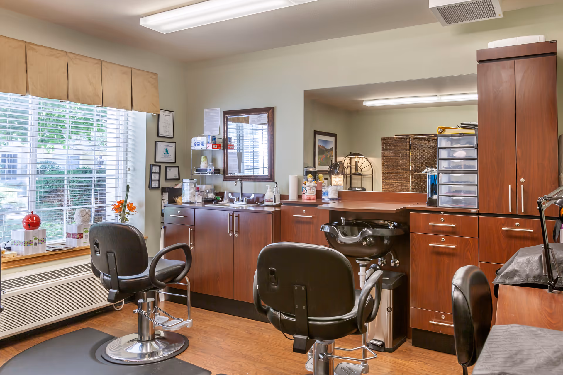 An interior salon area with styling chairs, a shampoo sink, wooden cabinets and a large window with blinds.