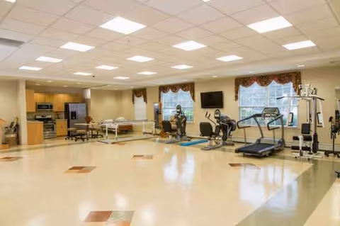 Bright fitness center in a senior living facility with treadmills and elliptical machines.