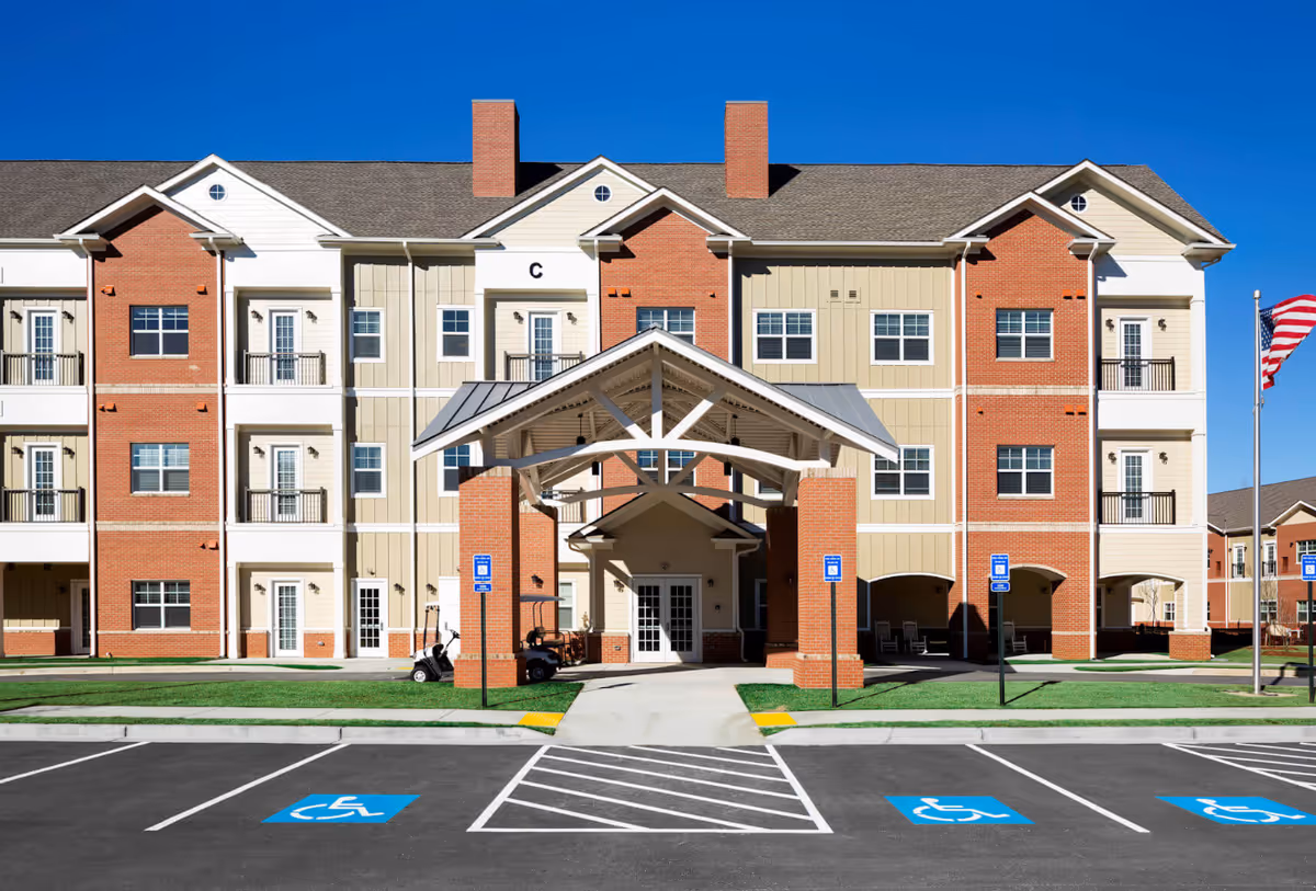 Three-story brick and beige senior living building with a covered entrance and handicap parking.