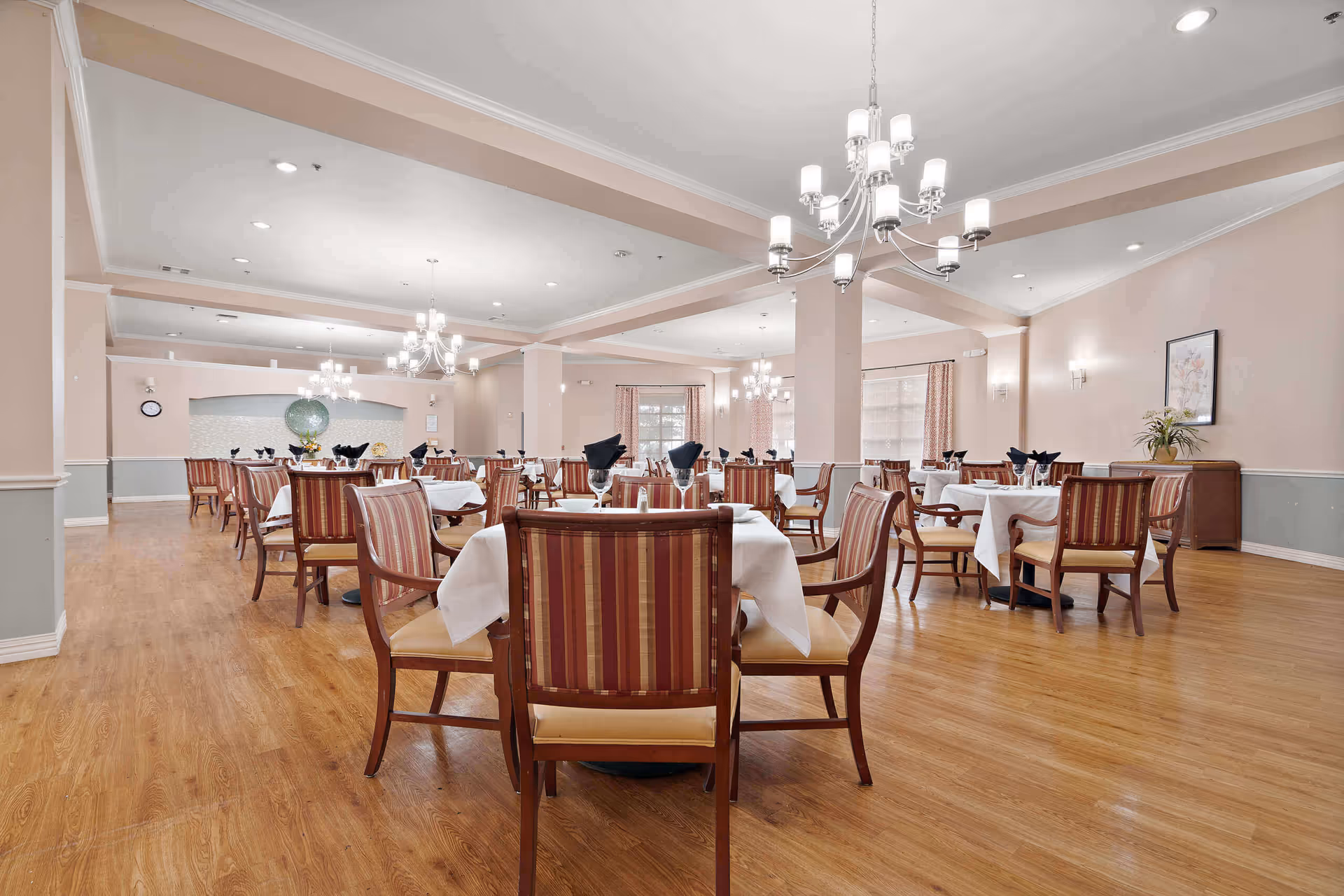 Spacious dining room with multiple tables set with white linens, striped chairs, and chandeliers.