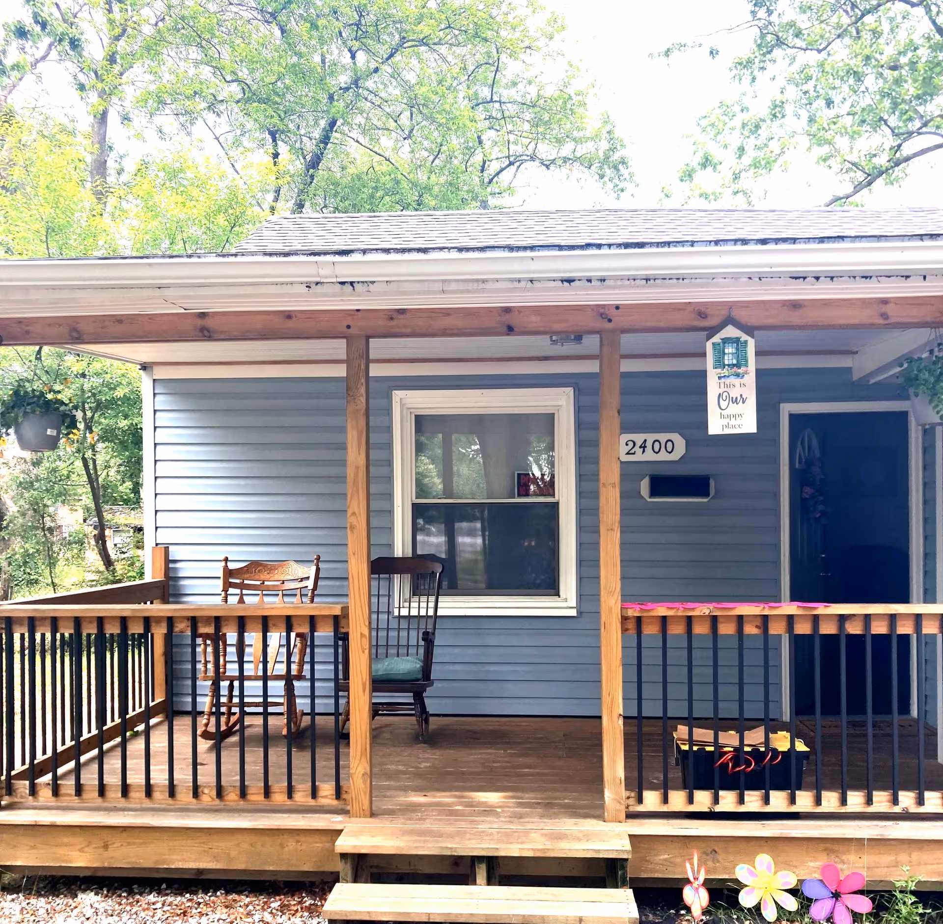 Front porch of a blue house with wooden posts and railing, two rocking chairs, and house number 2400.