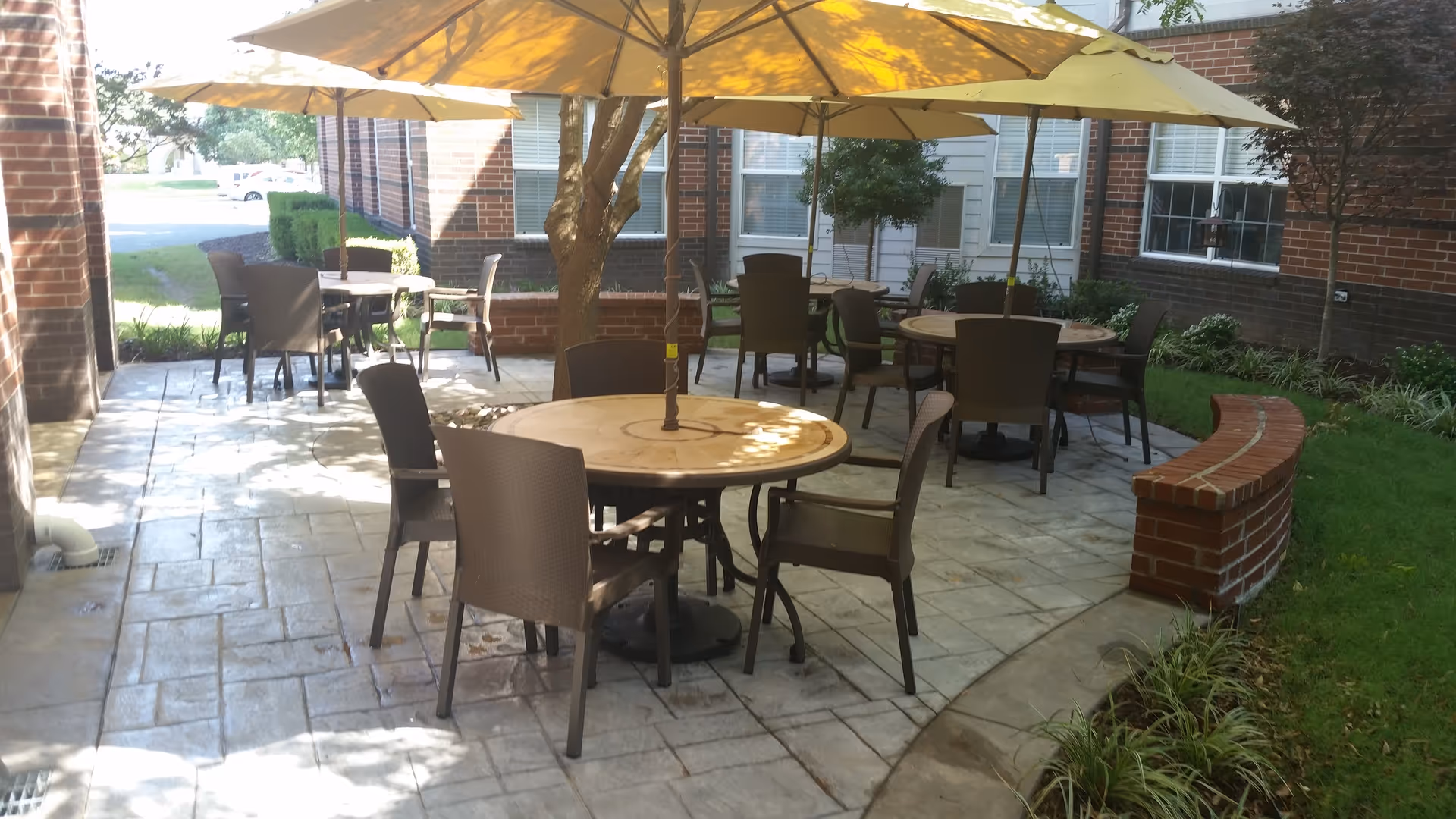 Outdoor patio with round tables, brown chairs and yellow umbrellas beside a brick building.