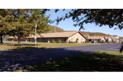 A single-story senior living facility exterior with a parking lot and surrounding trees.