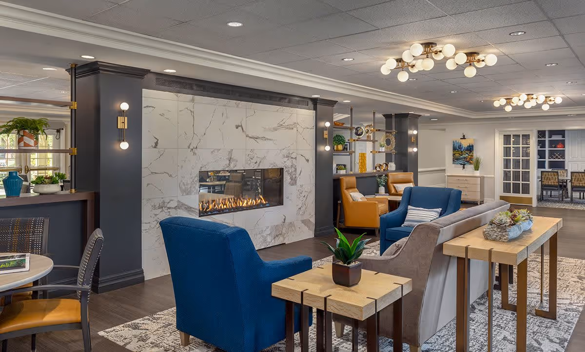 Bright communal lounge with modern seating, a marble fireplace, and decorative lighting.