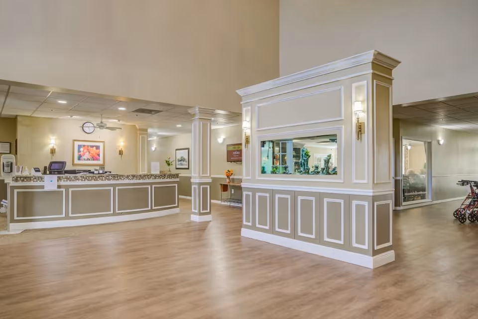 Lobby reception area with a front desk, decorative aquarium partition, and seating in a senior living facility.