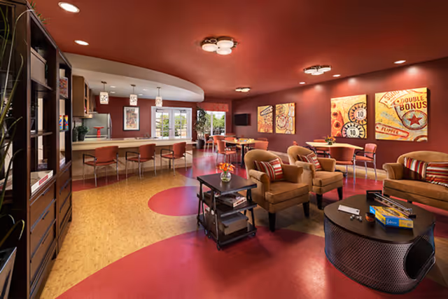 Spacious warm-toned common lounge with armchairs, tables, a dining counter, and colorful wall art.