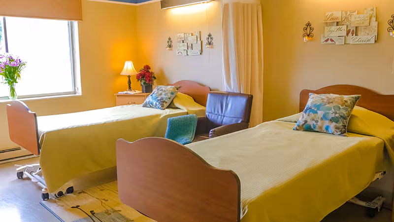 A bright shared bedroom with two single beds, a chair, bedside tables, and decorative wall art.