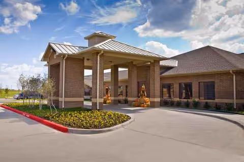 Brick senior living facility exterior with a covered entrance and autumn pumpkins.