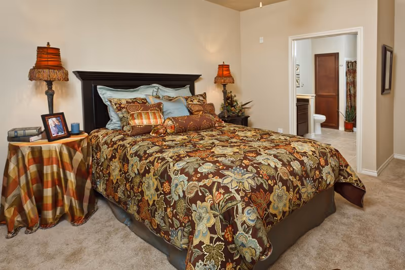 Bedroom featuring a large bed with patterned floral bedding, bedside tables and lamps, and an open door leading to a bathroom.