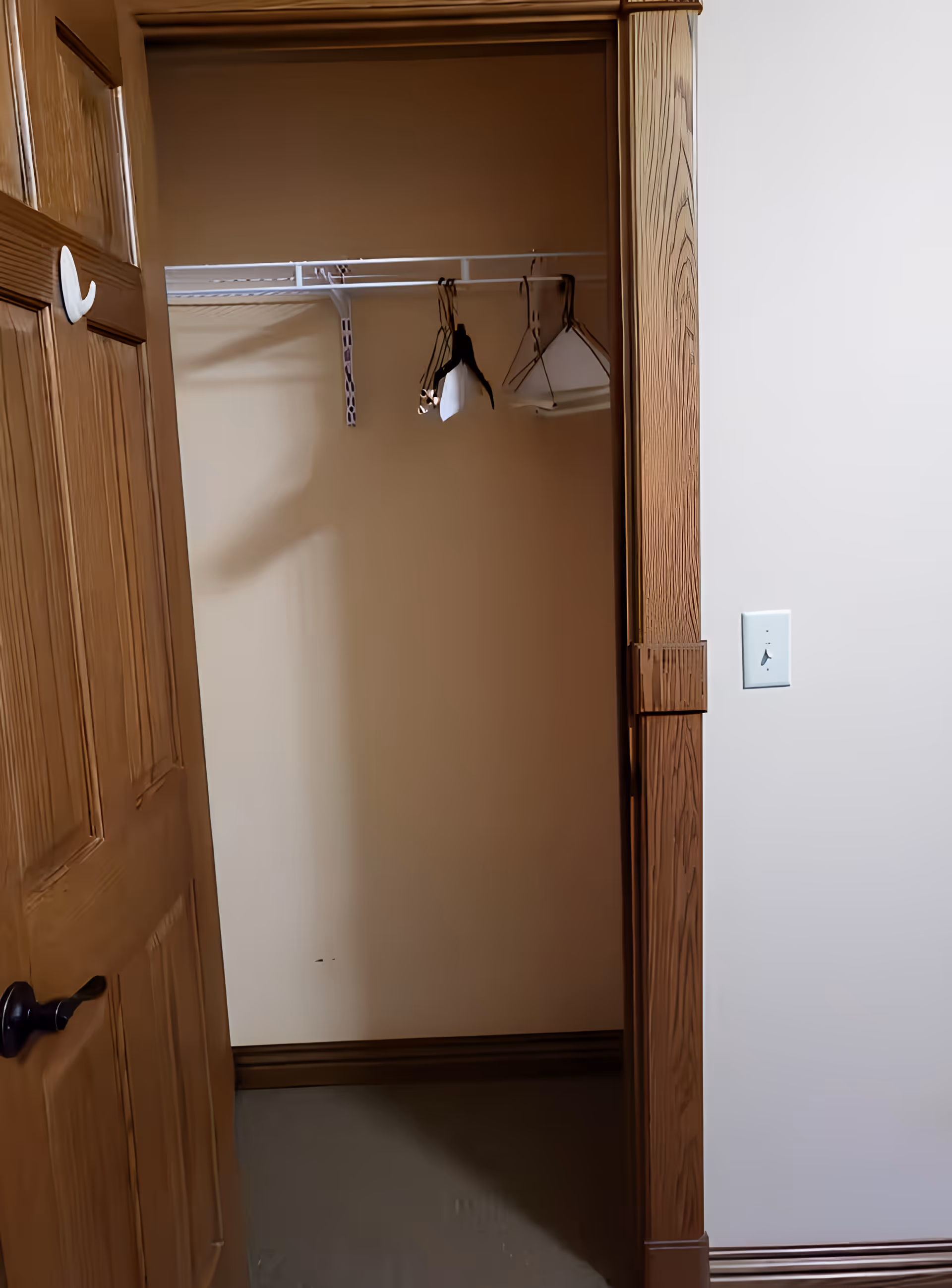Open wooden closet with a few hangers on a wire shelf inside a room.
