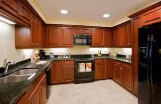 Well-equipped kitchen with dark wood cabinets, black appliances, granite countertops, and a sink.