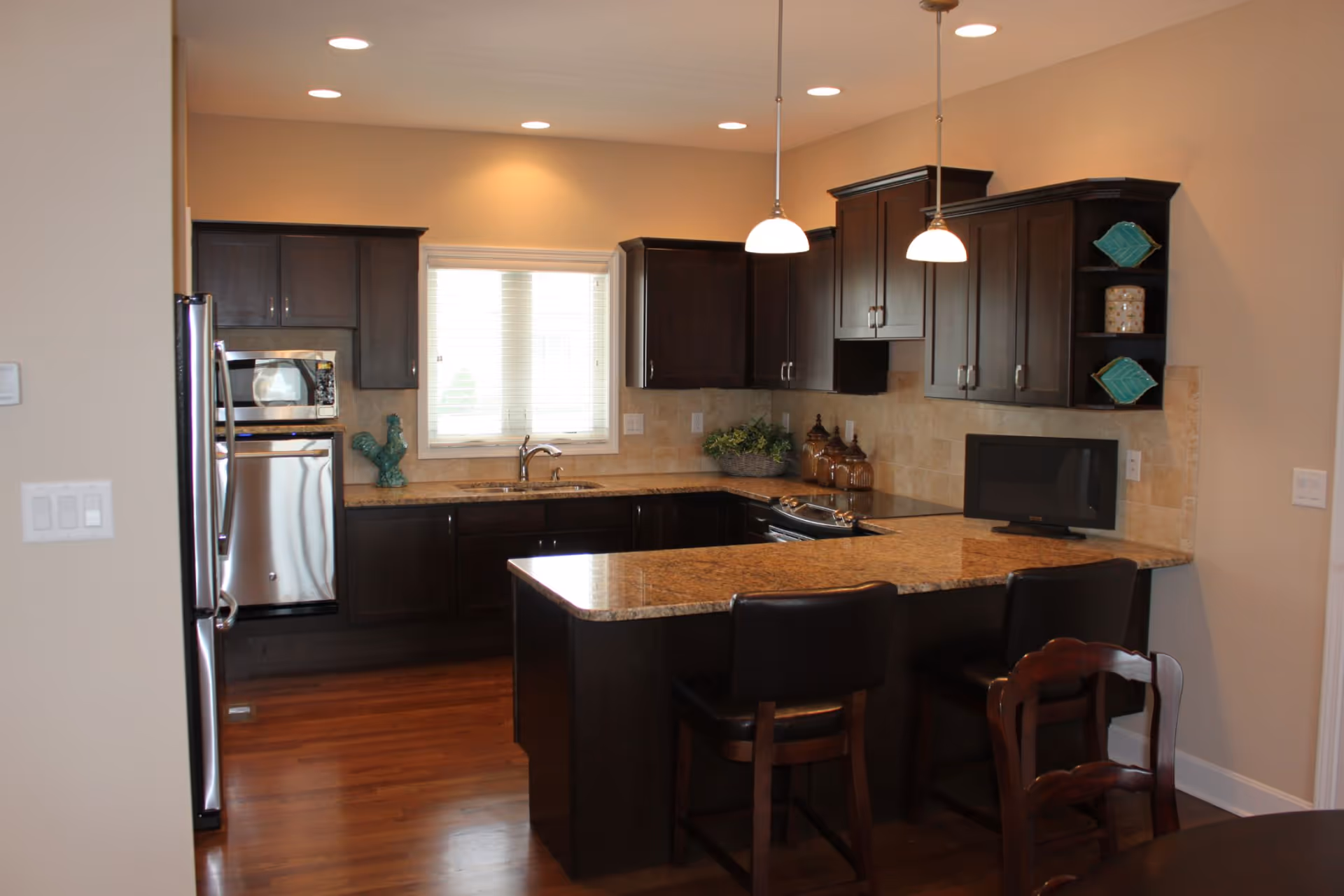 Modern kitchen with dark wood cabinets, a granite island with bar stools, stainless steel appliances, and pendant lights.