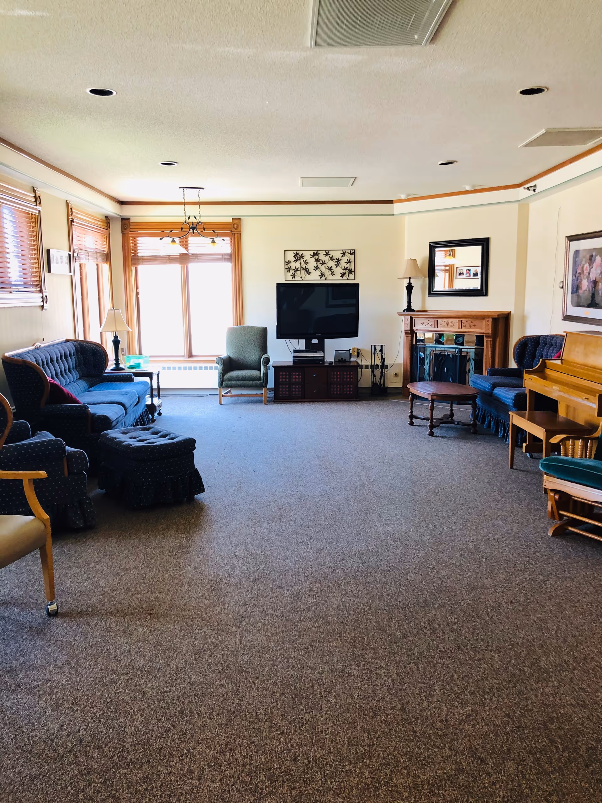 Bright communal living room with sofas, armchairs, a TV, piano and fireplace.
