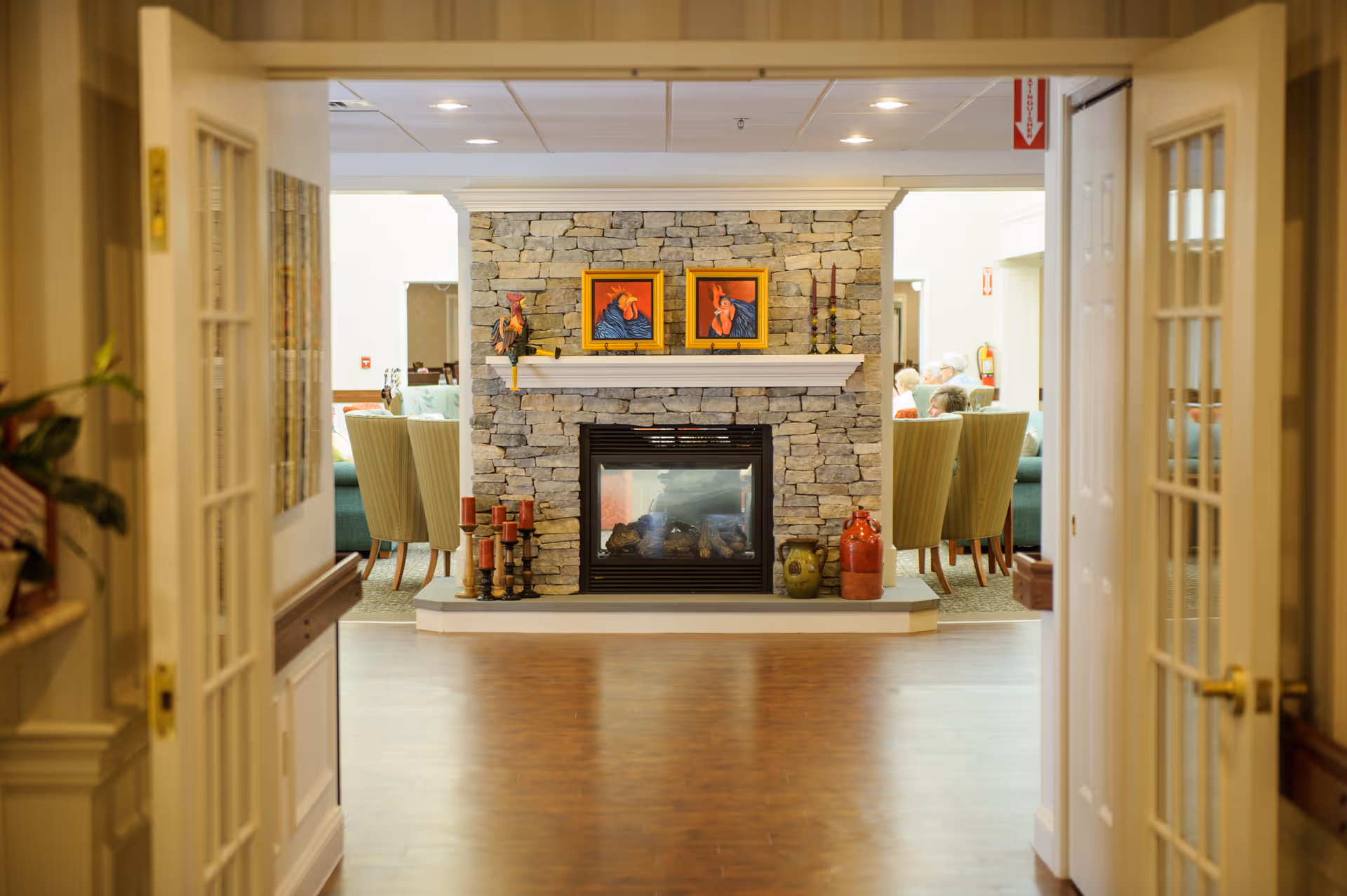 View through double doors into a cozy common lounge with a stone fireplace, seating, and decorative accents.