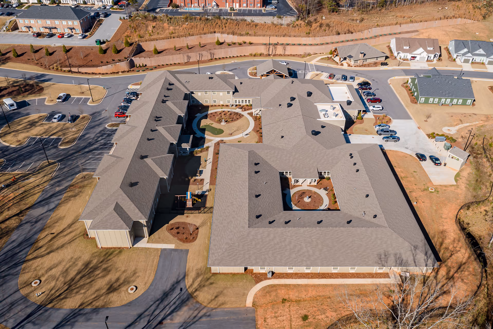 Aerial view of Oaks at Eagle's Landing senior living facility showing a large building complex with multiple wings, parking lots with cars, landscaped areas, and surrounding roads.
