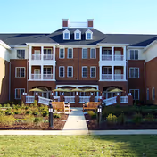 Brick senior living building with balconies and a central walkway leading to a lawn.