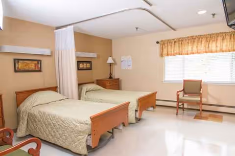 Two twin beds in a beige hospital-style bedroom with a privacy curtain and window.