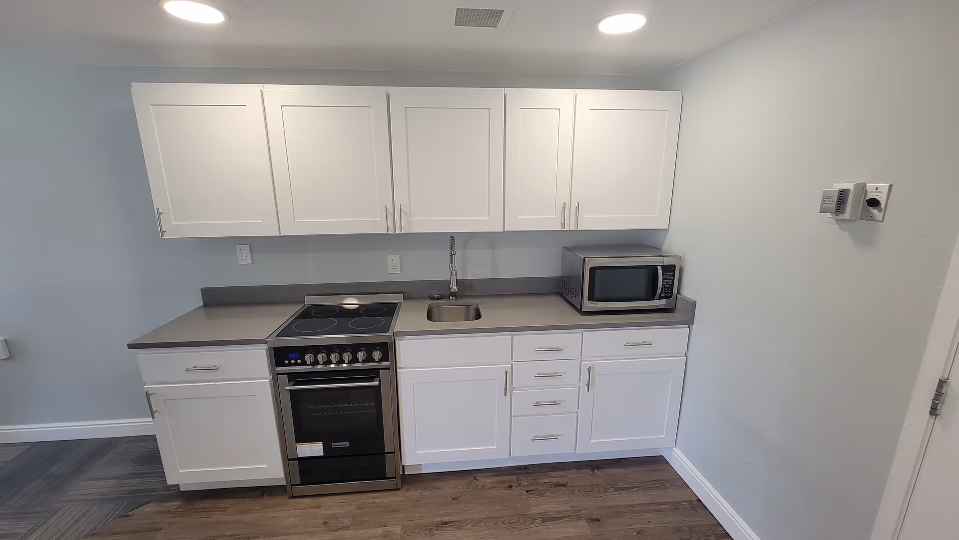 Small modern kitchenette with white cabinets, an electric range, sink, and a microwave on the countertop.