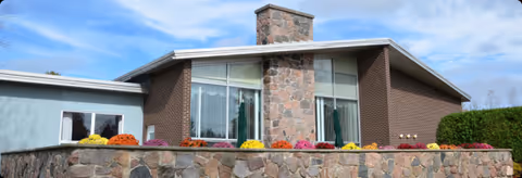Modern single-story brick building with stone accents and colorful flowers along a low wall.