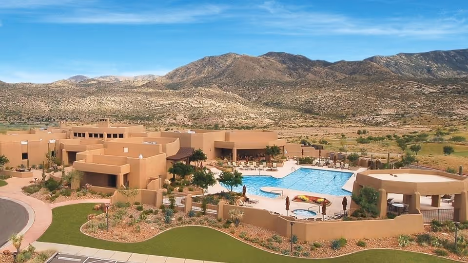 Aerial view of a southwestern-style senior living community with a central outdoor pool, patios, and desert landscaping set against nearby mountains.