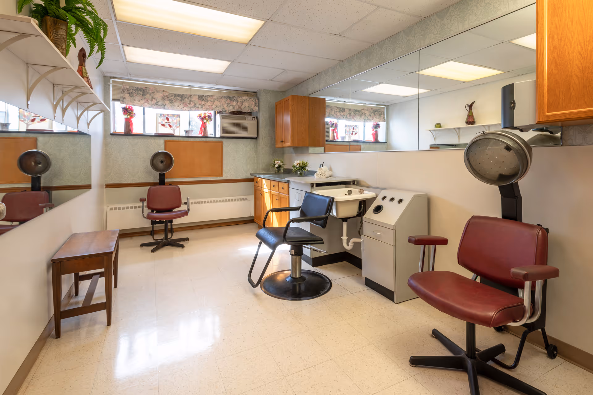 Small salon room with styling chairs, hooded hairdryers, a wash sink, cabinets and a large mirror.