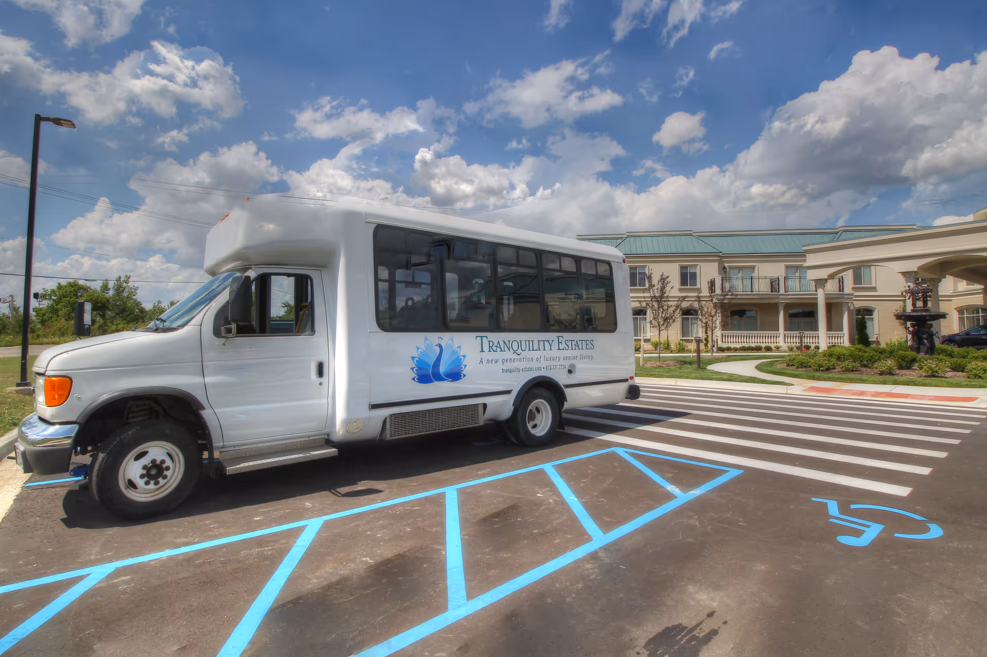 White Tranquility Estates shuttle bus parked in front of a senior living facility under a partly cloudy sky.