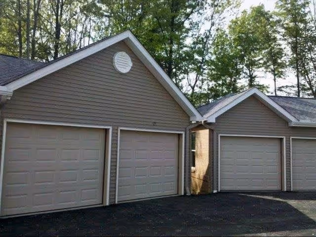 Exterior view of a building with three closed garage doors, surrounded by trees in the background.